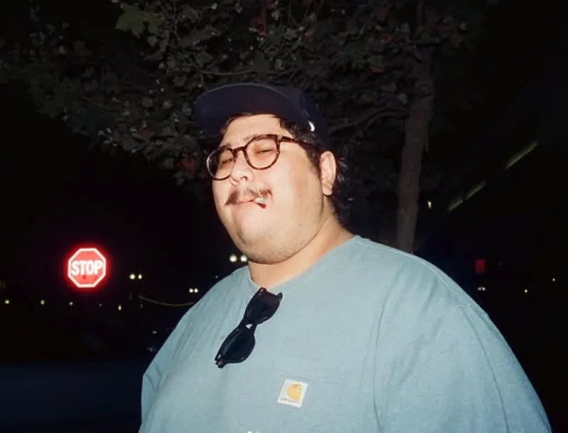Christian Gatica in a cap and glasses at night near a stop sign