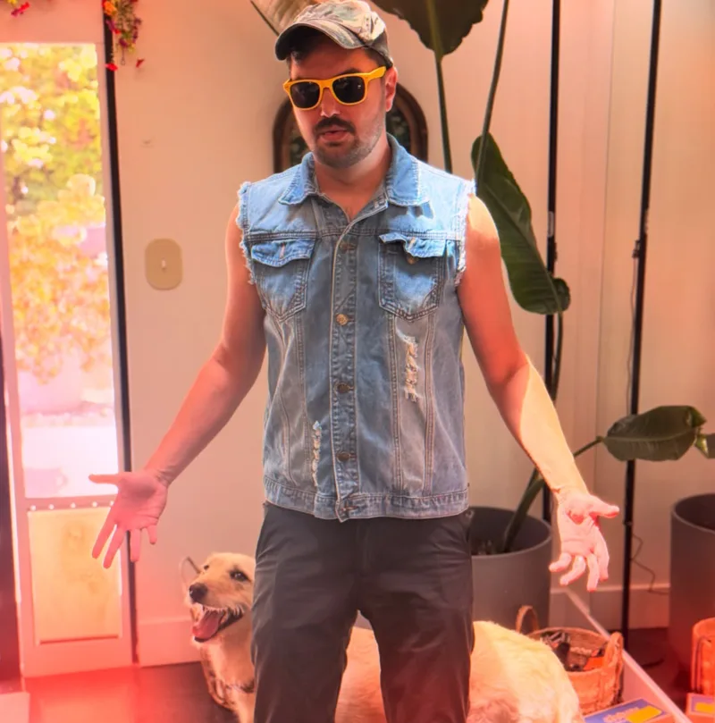 Elliott Morgan in a sleeveless denim vest and sunglasses, standing beside a dog