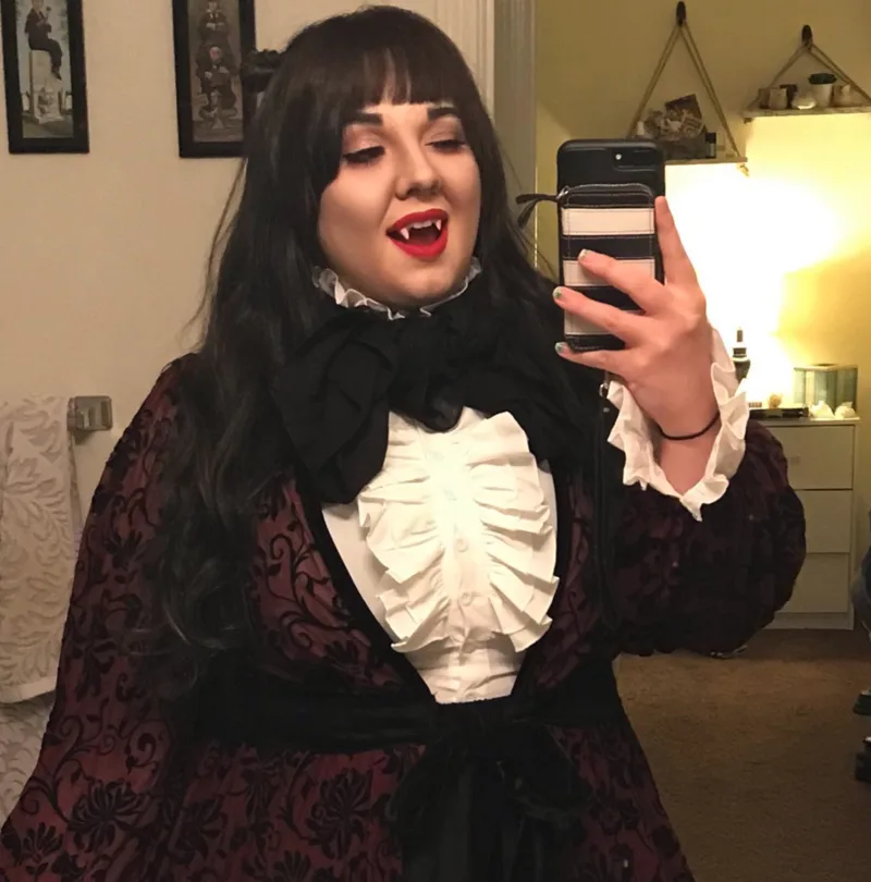 Felicia Schembari taking a mirror selfie in a vampire costume with a ruffled Victorian shirt
